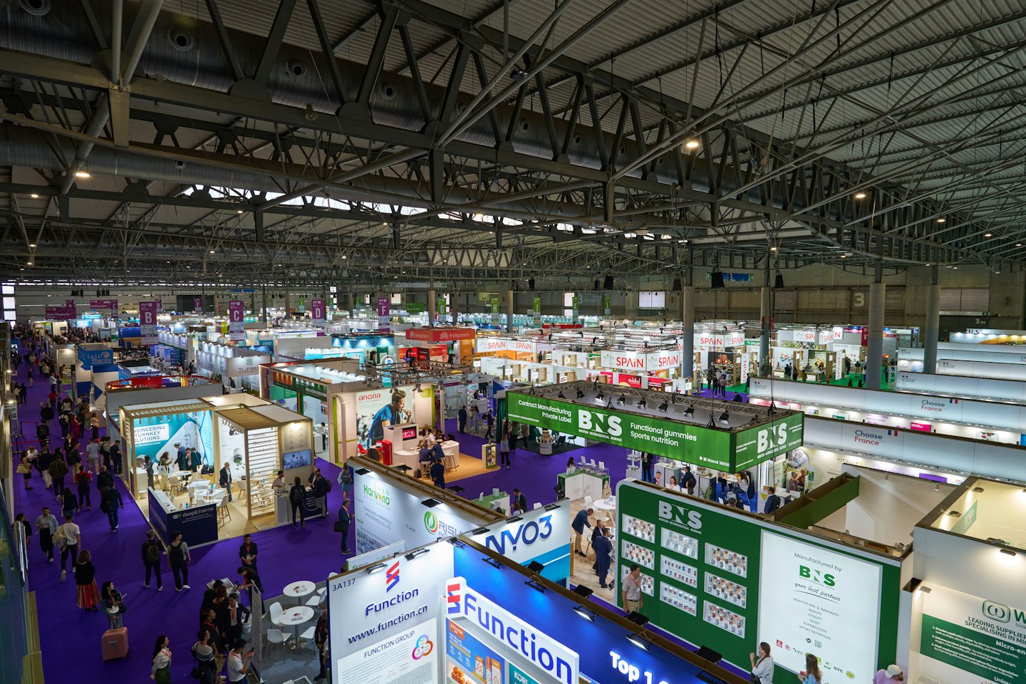 Attendees walk through aisles at a busy indoor trade show.